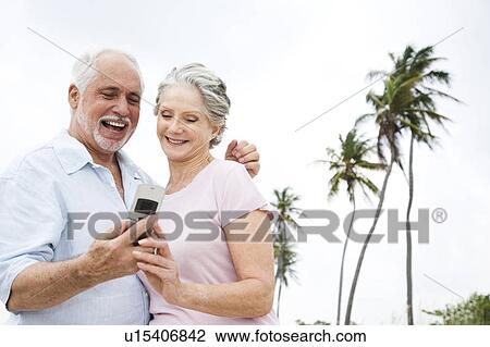 Stock Image - Senior couple looking at a mobile telephone at the beach . Fotosearch