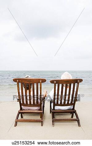 Picture - Senior couple relaxing in wooden steamer chairs at the beach . Fotosearch