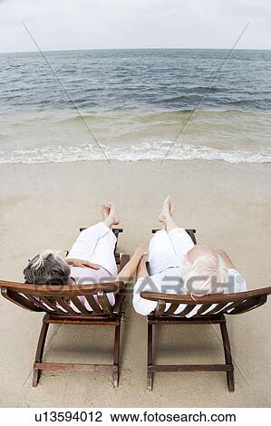 Senior couple relaxing in wooden steamer chairs at the beach View Large Photo Image Stock Image - Senior couple relaxing in wooden steamer chairs at the beach . Fotosearch
