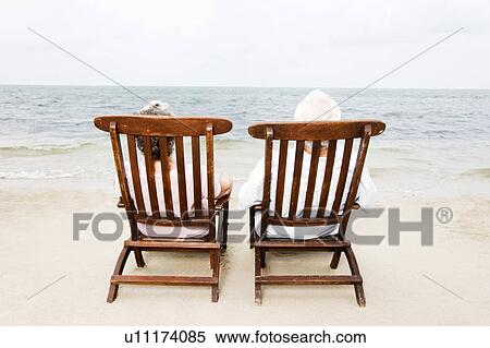 Stock Photography - Senior couple relaxing in wooden steamer chairs at the beach . Fotosearch
