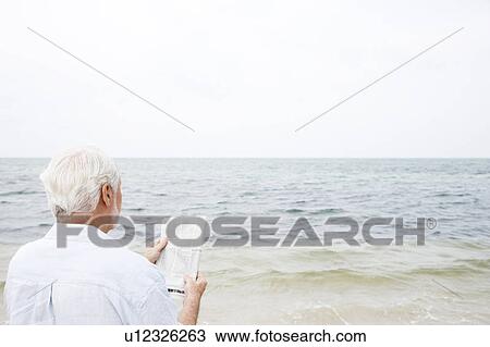Senior man at the beach reading a newspaper  View Large Photo Image Stock Image - Senior man at the beach reading a newspaper . Fotosearch