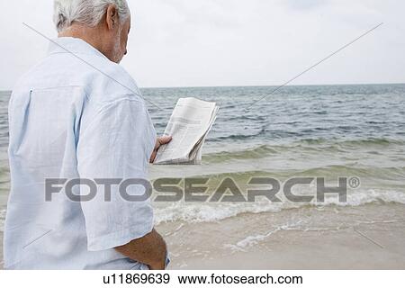 Stock Photo - Senior man at the beach reading a newspaper . Fotosearch
