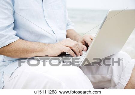 Stock Photo - Senior man at the beach using a laptop computer. Fotosearch