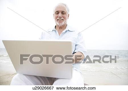 Senior man at the beach using a laptop computer View Large Photo Image Stock Photo - Senior man at the beach using a laptop computer. Fotosearch