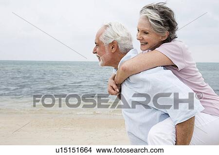 Picture - Senior man giving a senior woman a piggyback at the beach . Fotosearch