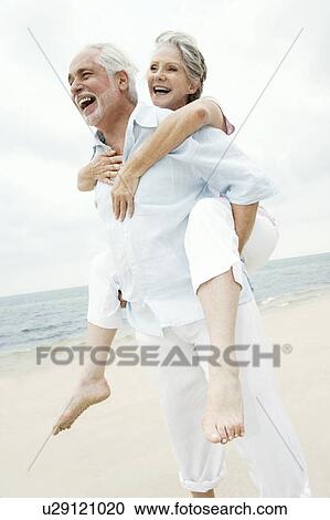 Senior man giving a senior woman a piggyback at the beach View Large Photo Image Stock Image - Senior man giving a senior woman a piggyback at the beach . Fotosearch