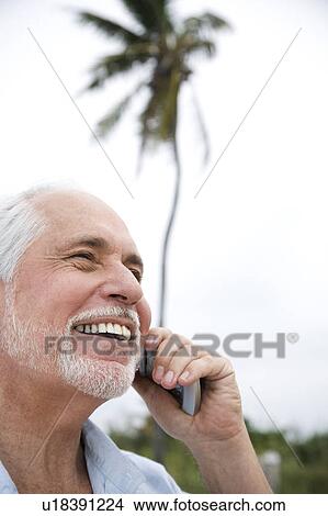 Picture - Senior man on a mobile telephone at the beach . Fotosearch