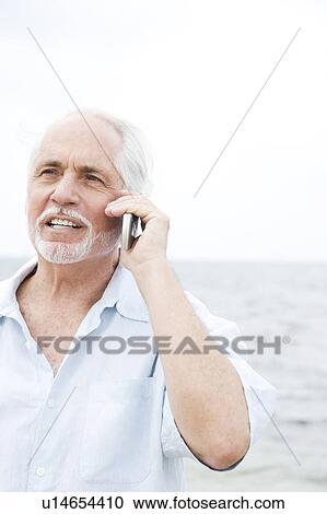 Stock Image - Senior man on a mobile telephone at the beach . Fotosearch