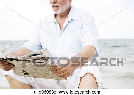 Stock Photography - Senior man sitting at the beach reading a newspaper . Fotosearch