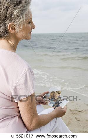 Stock Photo - Senior woman looking at photographs at the beach . Fotosearch