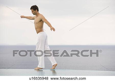 Stock Photo - A man balancing at the edge of a pool. Fotosearch