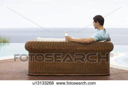Stock Photo - A man relaxing on a sofa by a pool. Fotosearch