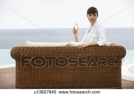 Stock Photography - A woman relaxing on a sofa by a pool. Fotosearch