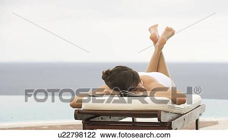 Stock Image - A woman relaxing on a sun lounger. Fotosearch