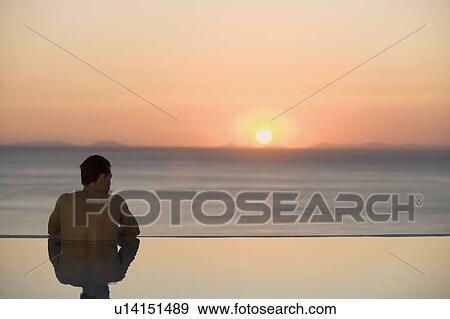Stock Photo - A man in a pool watching the sunset. Fotosearch
