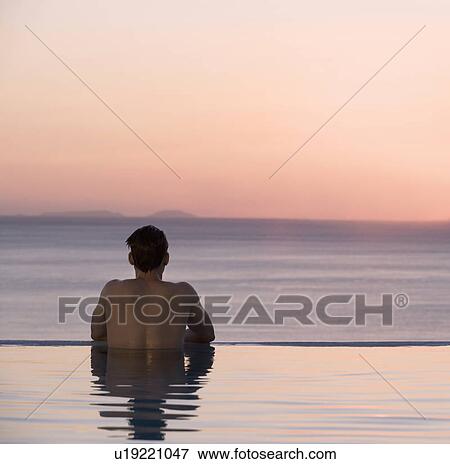 Stock Photo - A man in a pool watching the sunset. Fotosearch