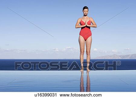 Stock Image - A woman meditating at the edge of a pool. Fotosearch