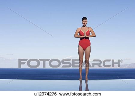 Stock Photograph - A woman meditating at the edge of a pool. Fotosearch