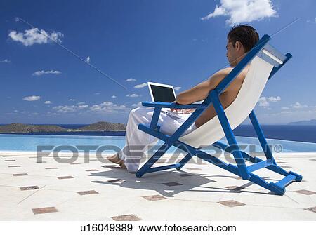 A man sitting on a deck chair using a laptop View Large Photo Image Stock Photo - A man sitting on a deck chair using a laptop. Fotosearch