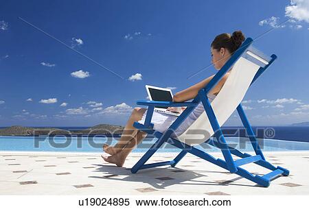 A woman sitting on a deck chair using a laptop View Large Photo Image Stock Photography - A woman sitting on a deck chair using a laptop. Fotosearch