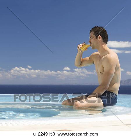 Stock Image - A man drinking fruit juice by a pool. Fotosearch