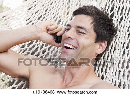 A man lying in a hammock chatting on a mobile phone View Large Photo Image Stock Photo - A man lying in a hammock chatting on a mobile phone. Fotosearch