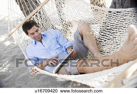 A man using a laptop whilst lying in a hammock View Large Photo Image Stock Image - A man using a laptop whilst lying in a hammock. Fotosearch