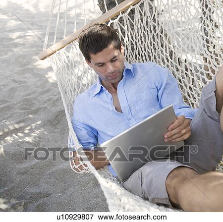 A man using a laptop whilst lying in a hammock View Large Photo Image Stock Photo - A man using a laptop whilst lying in a hammock. Fotosearch
