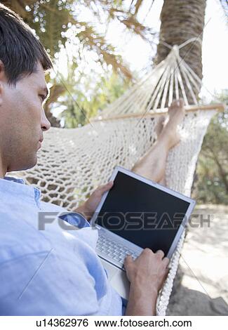 A man using a laptop whilst lying in a hammock View Large Photo Image Stock Photograph - A man using a laptop whilst lying in a hammock. Fotosearch