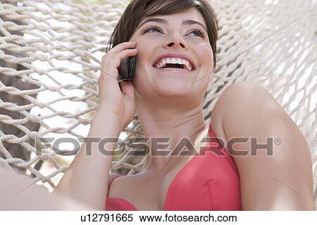 A woman lying in a hammock chatting on a mobile phone View Large Photo Image Stock Photography - A woman lying in a hammock chatting on a mobile phone. Fotosearch