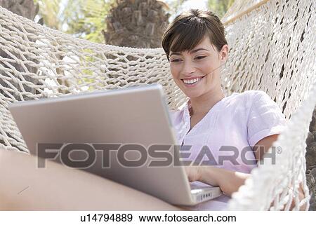 Stock Photo - A woman using a laptop lying in a hammock. Fotosearch