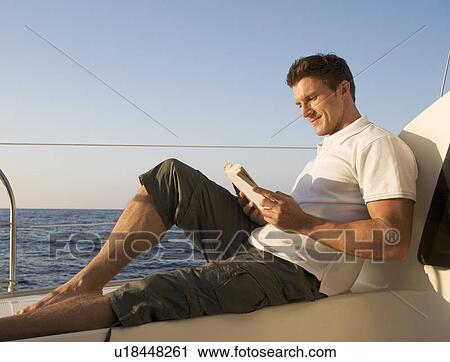 Stock Image - A man relaxing with a book on a boat. Fotosearch