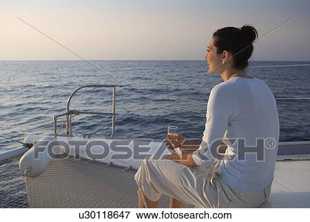 Stock Photo - A woman relaxing with a drink on a boat. Fotosearch