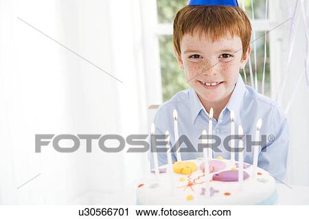 Stock Image - boy sitting at table with birthday cake. Fotosearch
