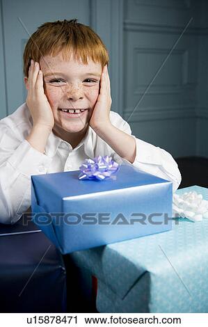 Stock Image - boy smiling sitting at table full of presents. Fotosearch