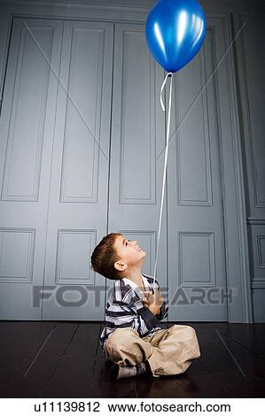 Stock Image - little boy sitting on the floor holding a balloon. Fotosearch