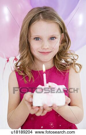 Picture - little girl in party dress holding miniature birthday cake. Fotosearch