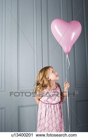little girl in party dress looking at her pink heart shaped balloon View Large Photo Image Stock Image - little girl in party dress looking at her pink heart shaped balloon. Fotosearch