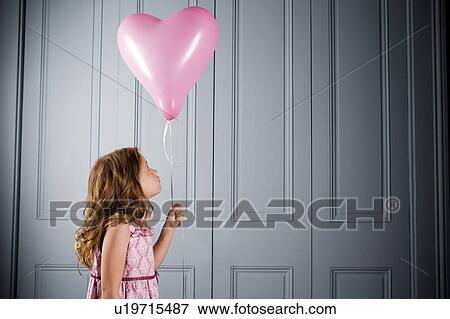 Stock Photo - little girl in party dress looking at her pink heart shaped balloon. Fotosearch