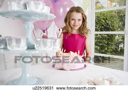 Stock Image - little girl standing in front of birthday cake on tea table. Fotosearch