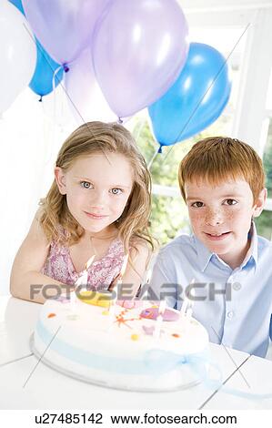 Stock Image - two children sitting at table with birthday cake. Fotosearch
