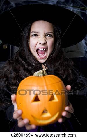Girl in a witch's costume at a Halloween party holding a pumpkin with a carved face View Large Photo Image Picture - Girl in a witch's costume at a Halloween party holding a pumpkin with a carved face. Fotosearch