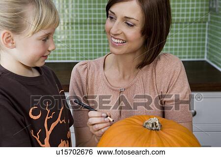 Stock Photograph - Mother and daughter carving a face in a Hallowe'en pumpkin. Fotosearch