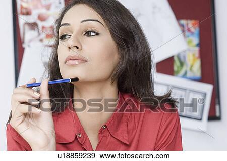 Stock Photo - Close-up of a female fashion designer holding a pencil and thinking. Fotosearch