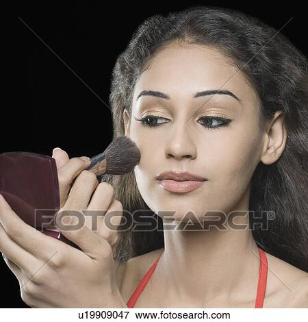 Stock Photo - Close-up of a young woman applying blush on her face. Fotosearch