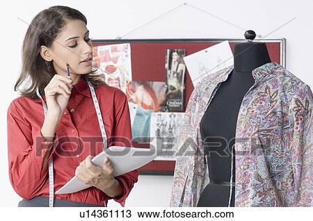 Stock Image - Fashion designer looking a mannequin and holding documents. Fotosearch
