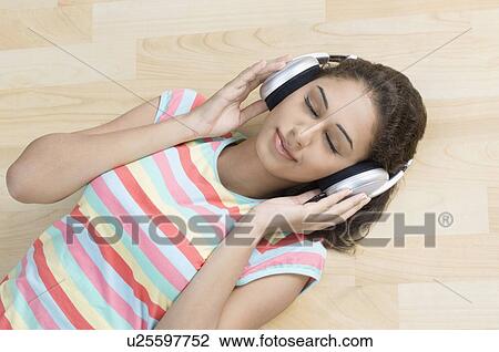 High angle view of a young woman lying on the hardwood floor and listening to music View Large Photo Image Stock Image - High angle view of a young woman lying on the hardwood floor and listening to music. Fotosearch