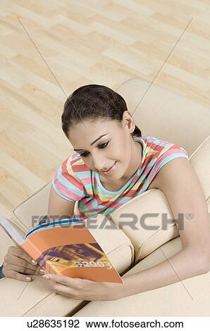 High angle view of a young woman sitting on a couch and reading a magazine View Large Photo Image Stock Image - High angle view of a young woman sitting on a couch and reading a magazine. Fotosearch