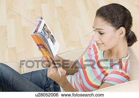 High angle view of a young woman sitting on a couch and reading a magazine View Large Photo Image Stock Photograph - High angle view of a young woman sitting on a couch and reading a magazine. Fotosearch