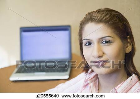 Stock Image - Portrait of a businesswoman smiling with a laptop in the background. Fotosearch